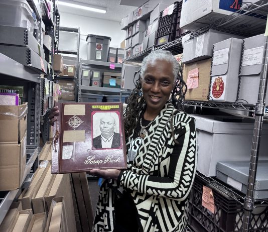DSC director and director of collections Michelle Jahra McKinney holds up a scrapbook from the DSC archives, currently housed in Detroit’s WGPR 107.5 FM building.