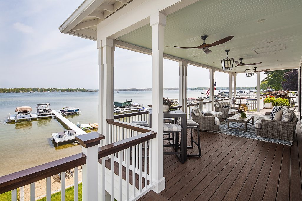 A covered deck patio with furniture and ceiling fans near a boat dock on a lake.