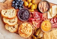 A charcuterie board with bread, meat, dips, fruit, and other snacks.