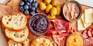 A charcuterie board with bread, meat, dips, fruit, and other snacks.