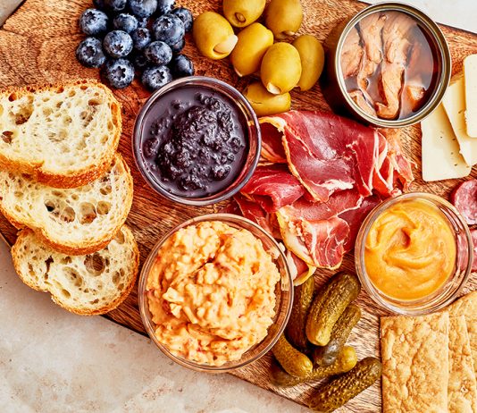A charcuterie board with bread, meat, dips, fruit, and other snacks.