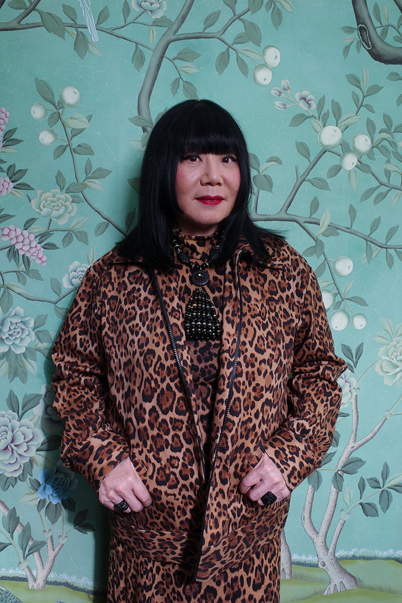 Anna Sui posing in front of a floral background.