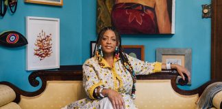 Sabrina Nelson sitting on a couch in front of a wall full of art.