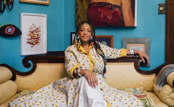 Sabrina Nelson and The Art of Dressing Sabrina Nelson sitting on a couch in front of a wall full of art.