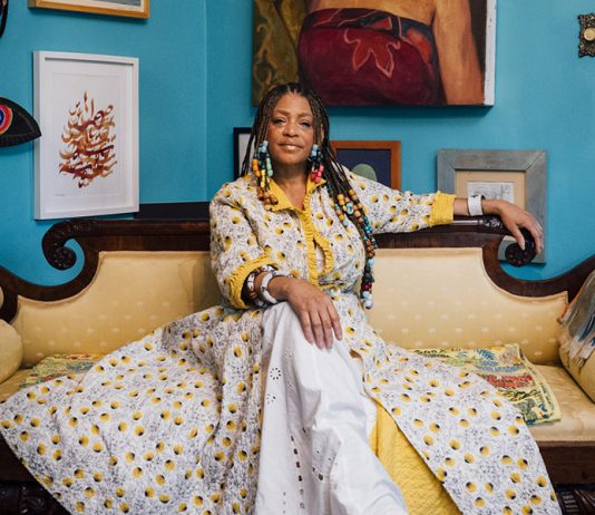 Sabrina Nelson sitting on a couch in front of a wall full of art.