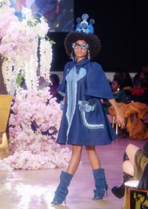 Caldonia&rsquo;s Box: A jutting knee-length denim dress with oversized bow, wide sleeves, and oversized pockets with blue contrasting trim and roses.